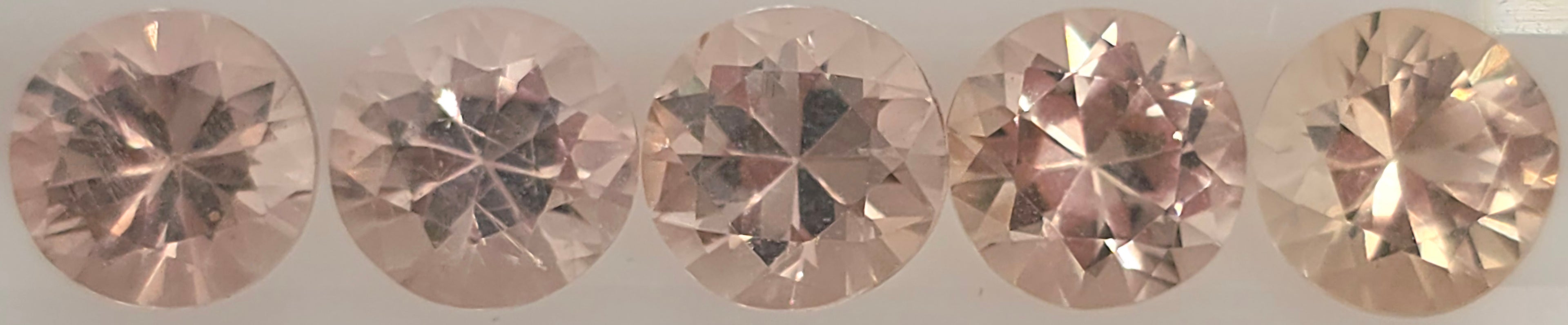 Five round brilliant-cut orangy pink to pinkish orange gemstones arranged in a row on a light gray background.