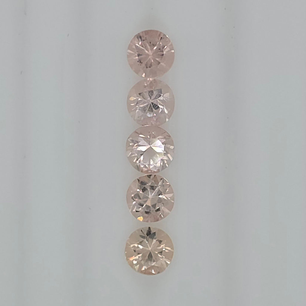 Five round-cut orangy pink to pinkish orange gemstones arranged vertically on a plain light background