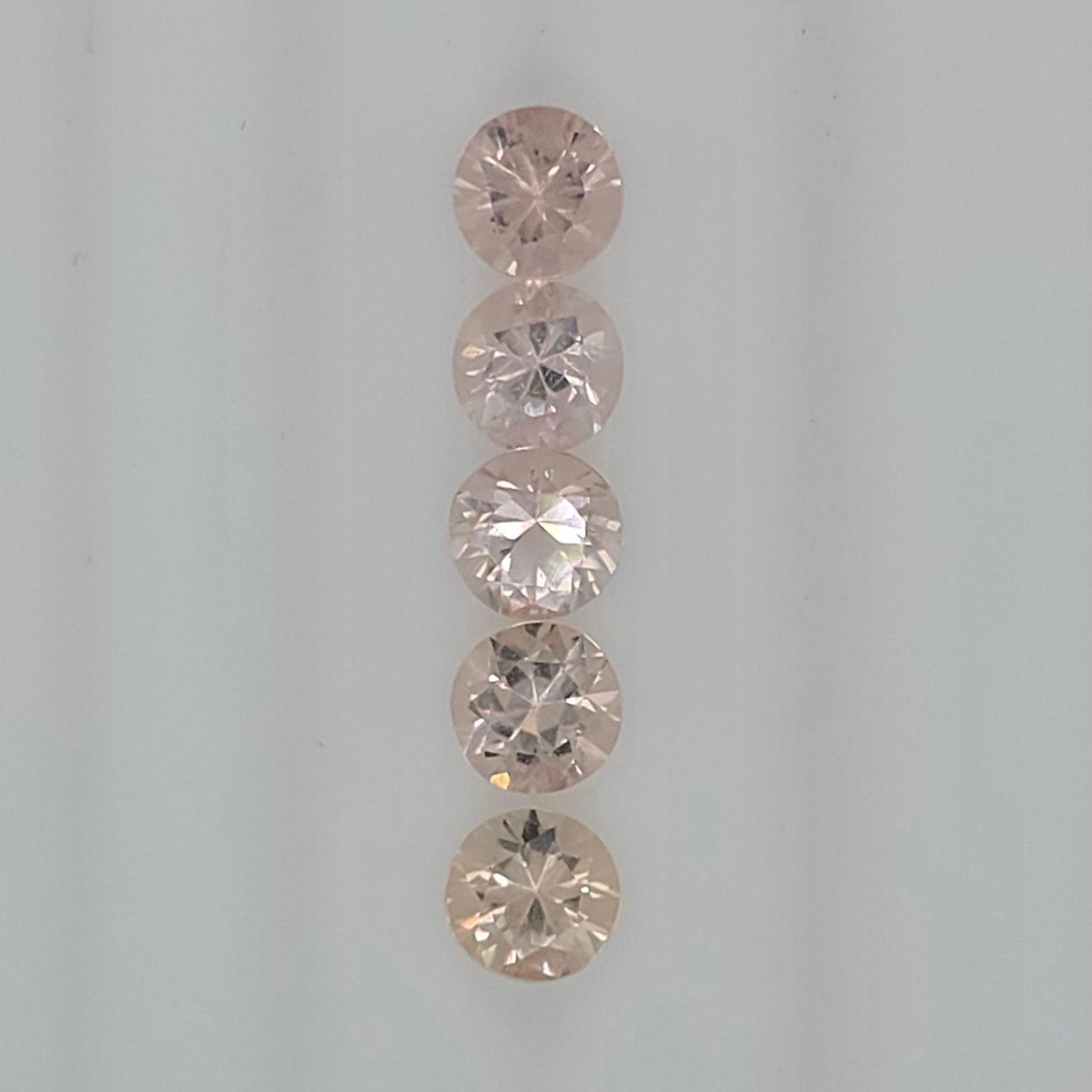 Five round-cut orangy pink to pinkish orange gemstones arranged vertically on a plain light background