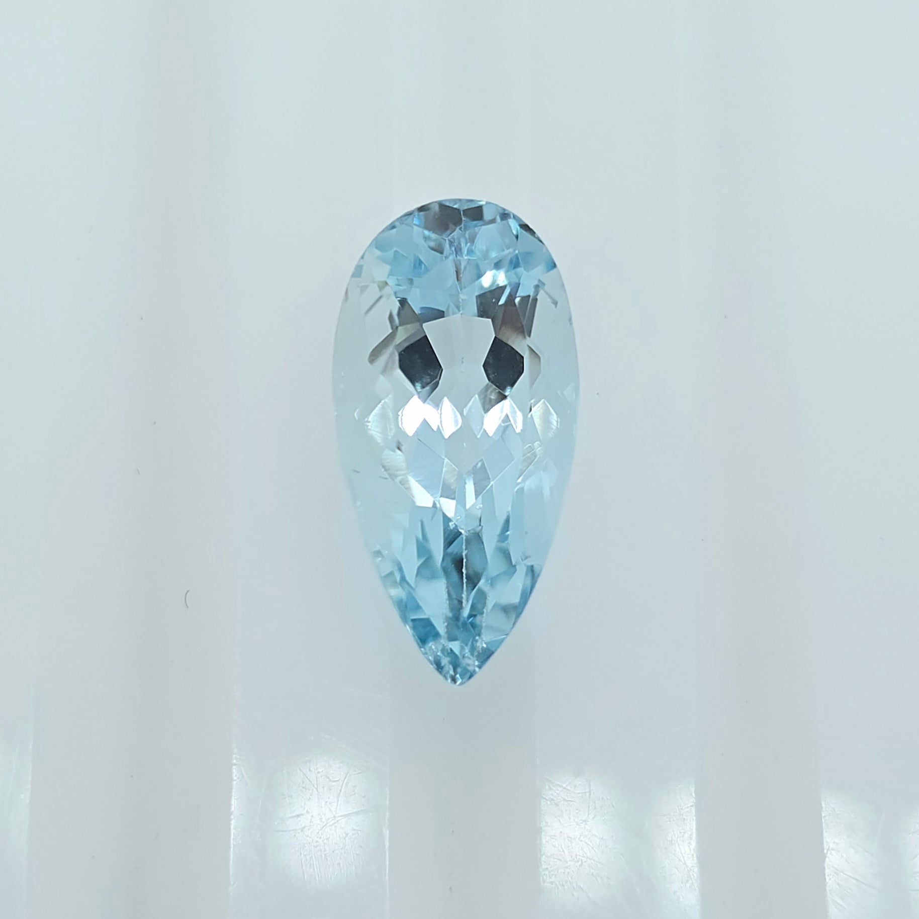 A single faceted pear-shaped light blue gemstone centered against a bright white background.