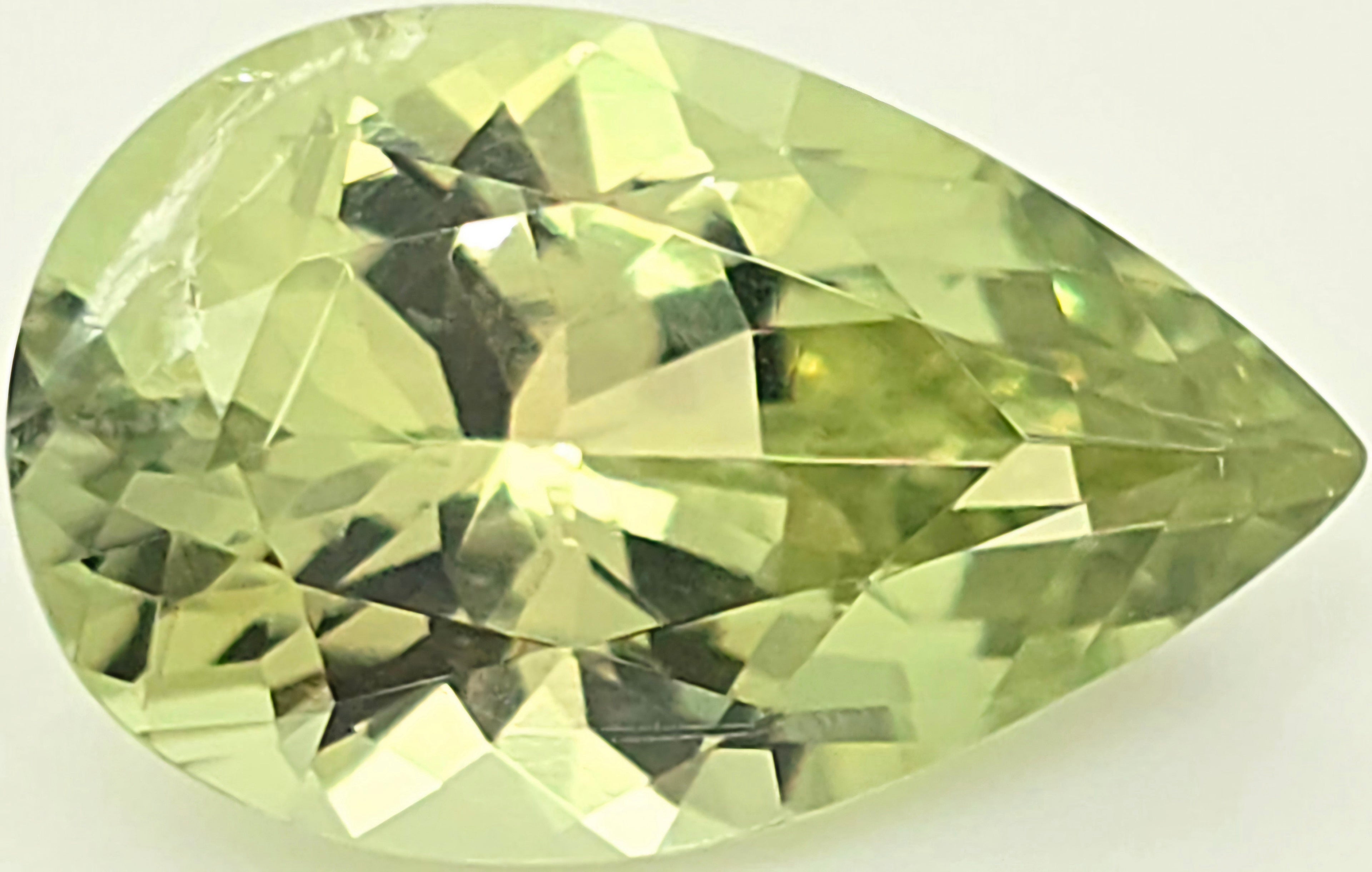 A faceted pear-cut gemstone with a lighter lime green color, displayed against a clean, off-white background.