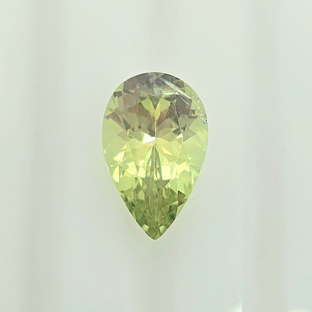 A faceted pear-cut gemstone with a lighter lime green color, displayed against a clean, off-white background.