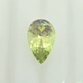 A faceted pear-cut gemstone with a lighter lime green color, displayed against a clean, off-white background.