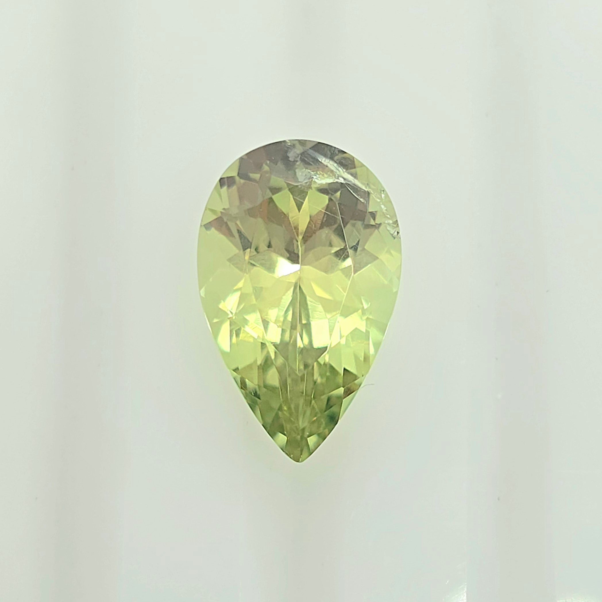 A faceted pear-cut gemstone with a lighter lime green color, displayed against a clean, off-white background.