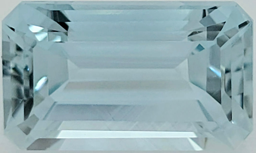 A rectangular emerald-cut light blue gemstone with a faceted, reflective surface, shown against a plain white background.