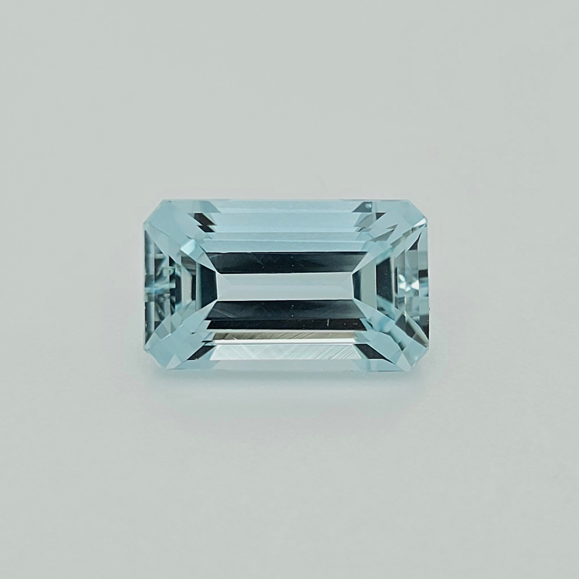 A light blue emerald-cut gemstone with a brilliant faceted finish, centered on a clean, light gray background.