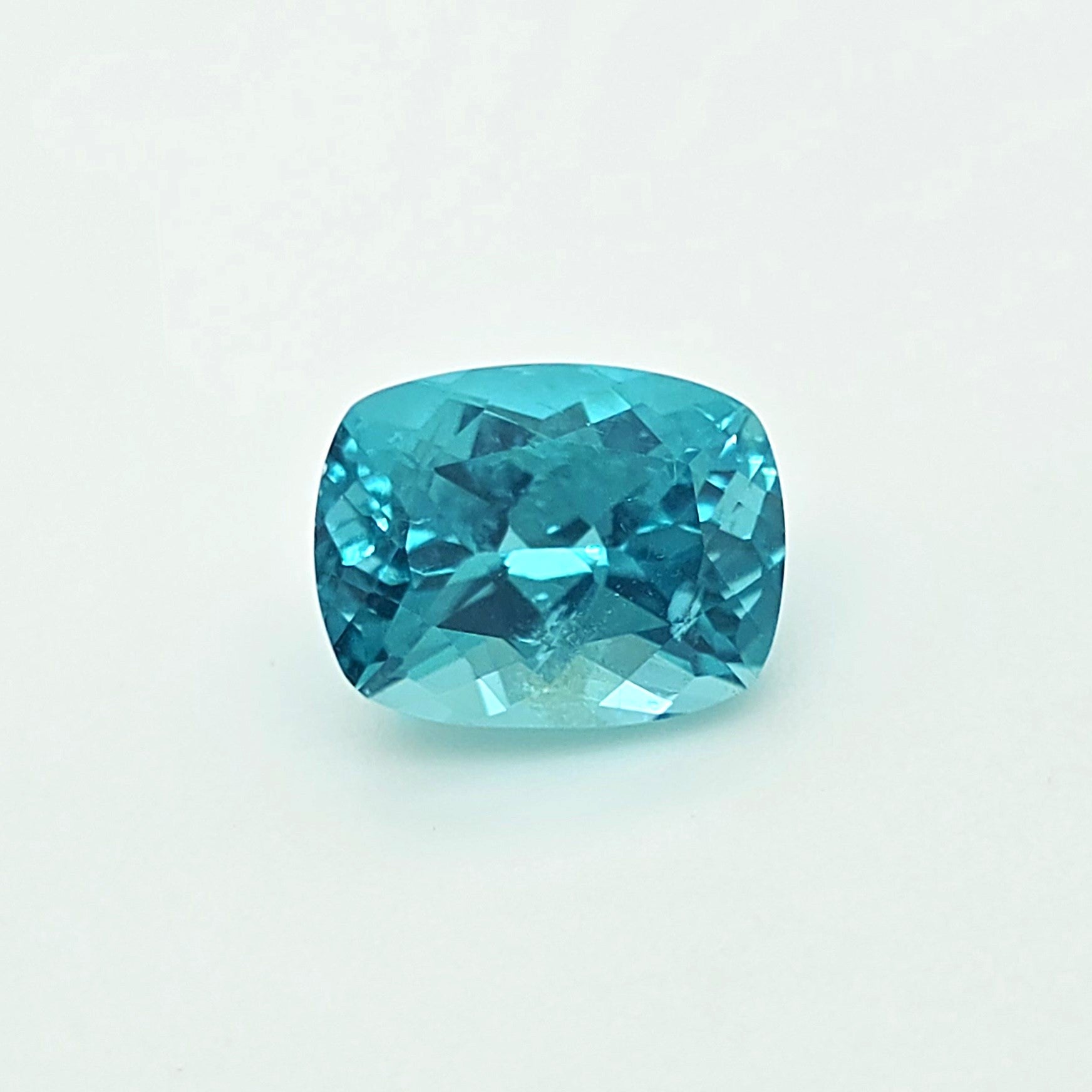 A cushion-cut blue gemstone with a faceted, brilliant cut, displayed on a clean white background.