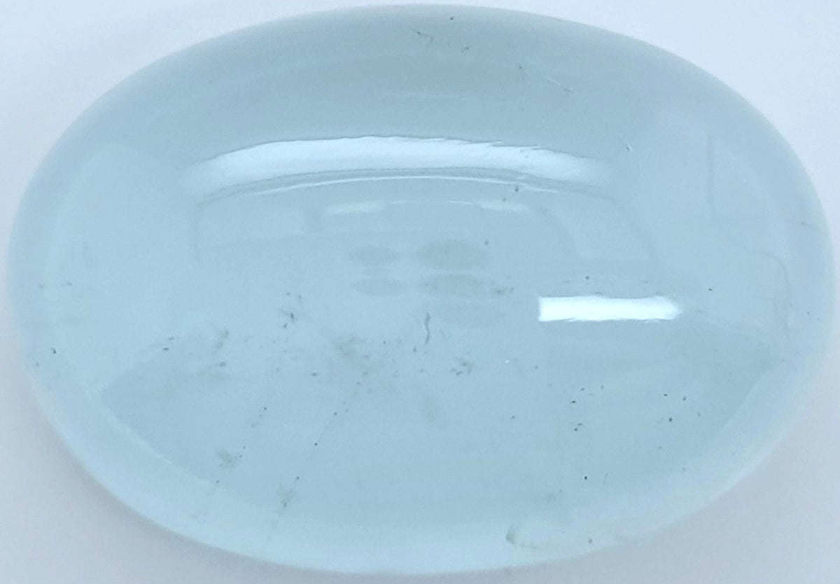 Close up of a polished oval light blue cabochon gemstone with natural inclusions on a white background