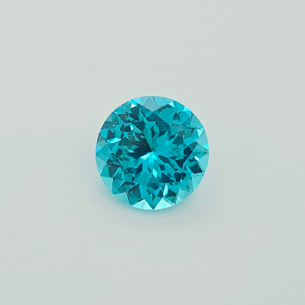 A round brilliant-cut greenish blue gemstone, centered on a clean, light gray background.