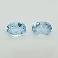 Two oval-cut light blue gemstones with faceted cuts, displayed side-by-side on a plain light gray background.