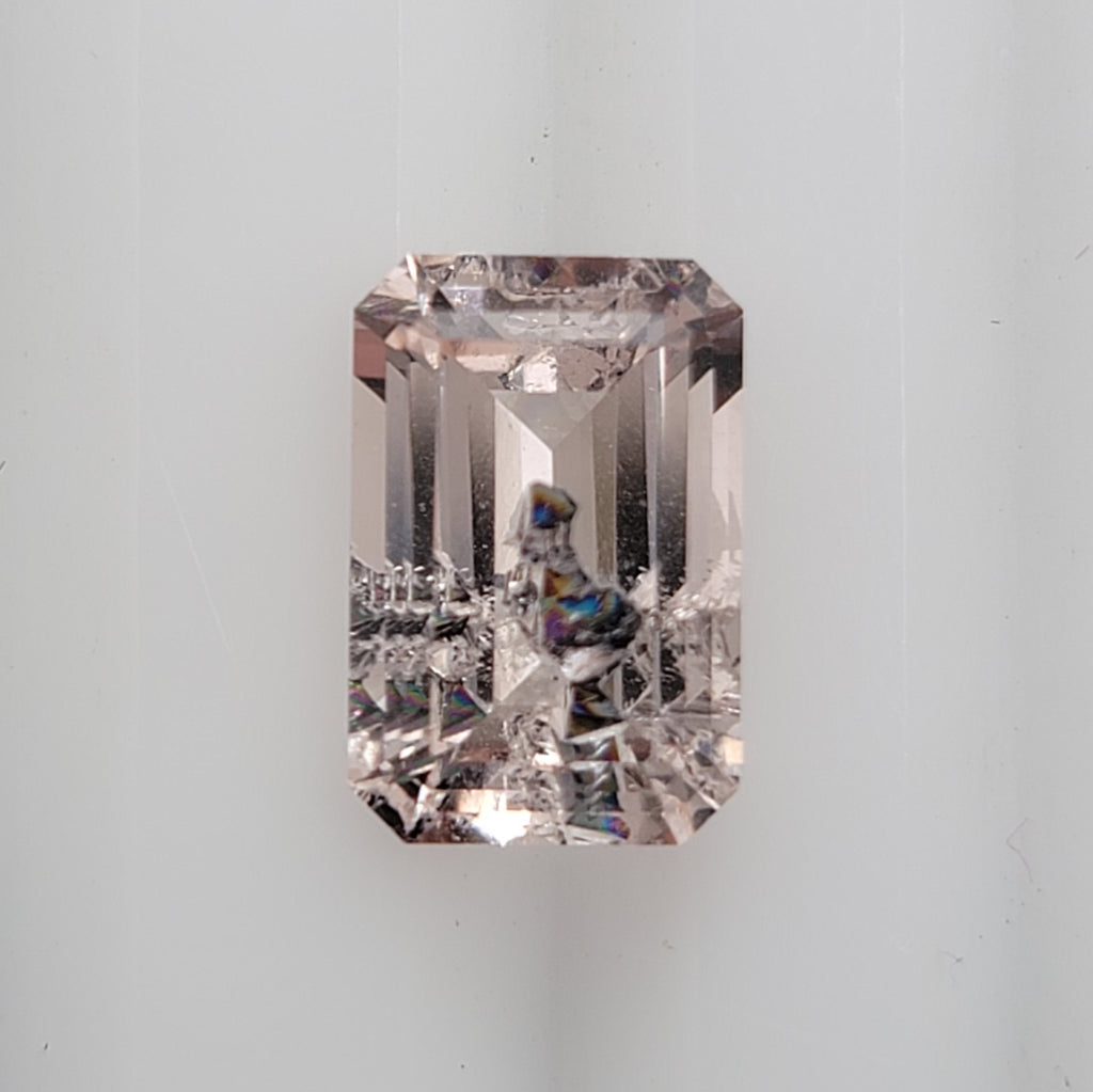 An emerald-cut pink gemstone with iridescent inclusion on a clean white background.