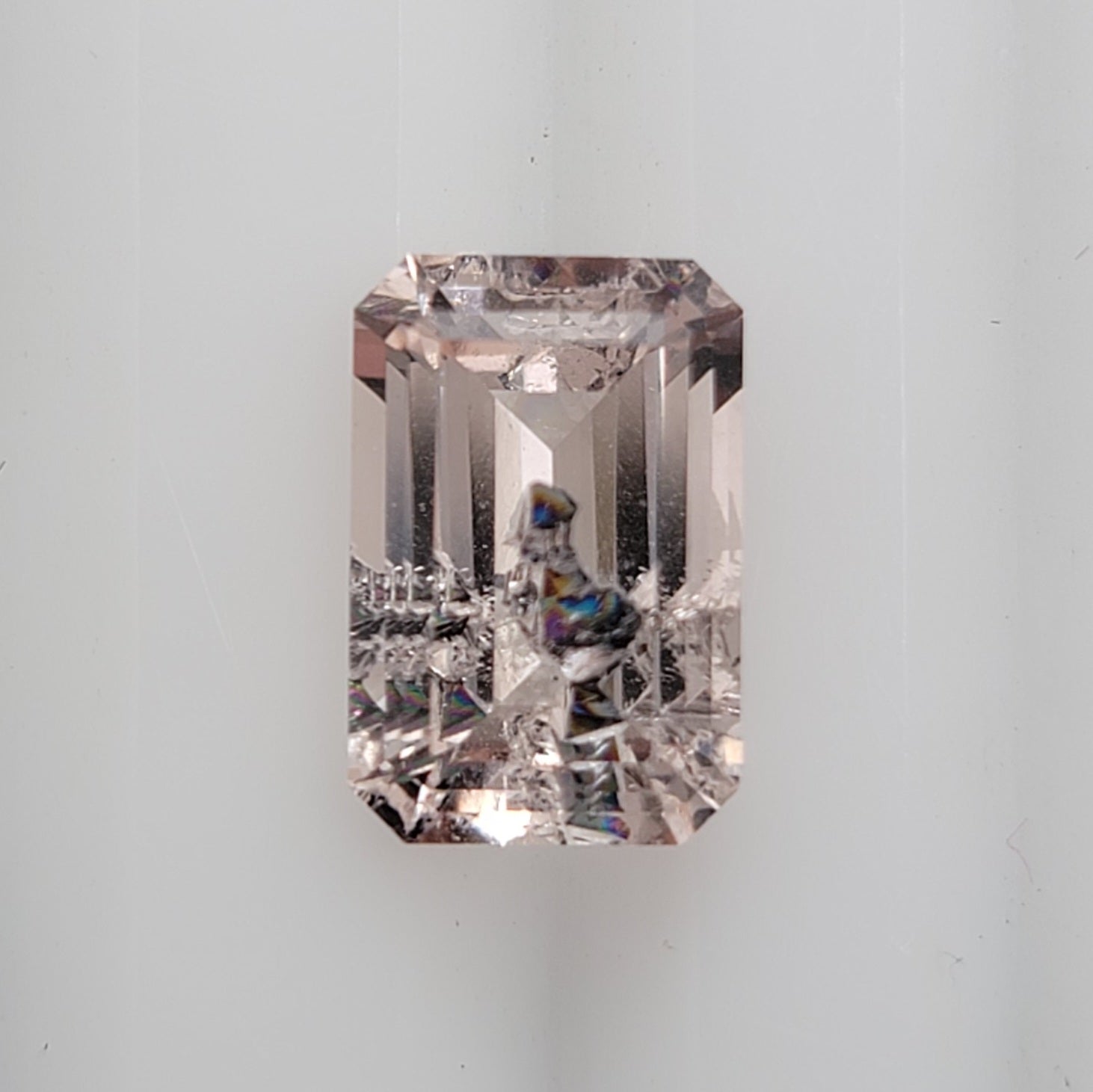 An emerald-cut pink gemstone with iridescent inclusion on a clean white background.