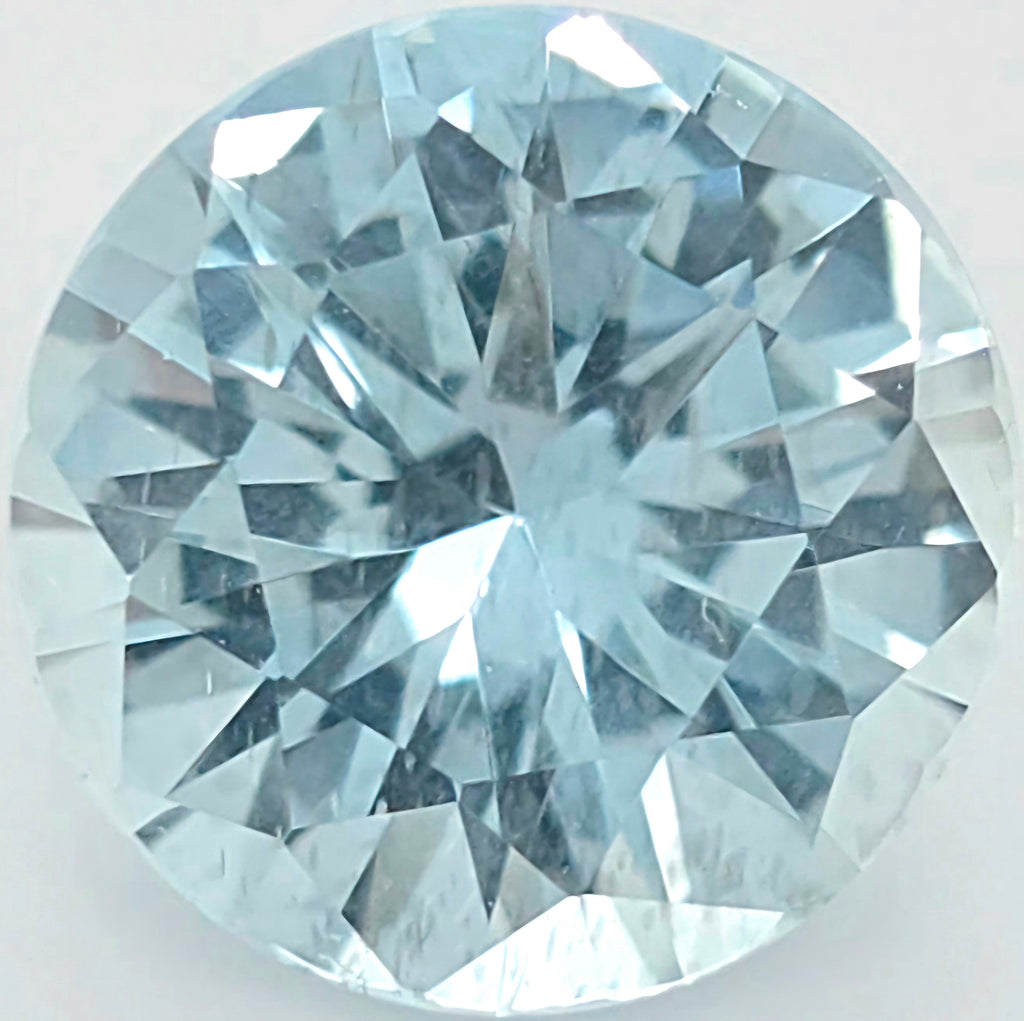 A round brilliant-cut light blue gemstone, showing detailed faceted reflections on a plain light background.
