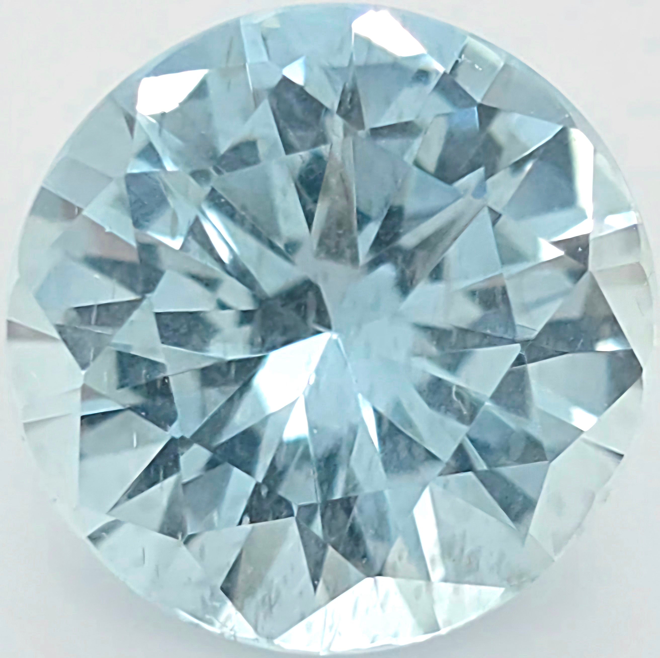 A round brilliant-cut light blue gemstone, showing detailed faceted reflections on a plain light background.