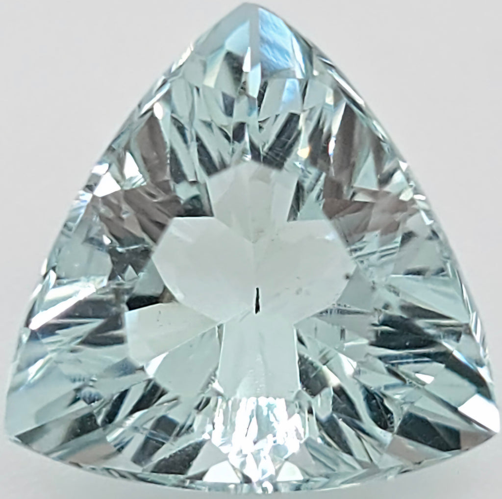 A triangular, faceted light greenish blue gemstone, shown in a close-up studio shot against a light gray background.