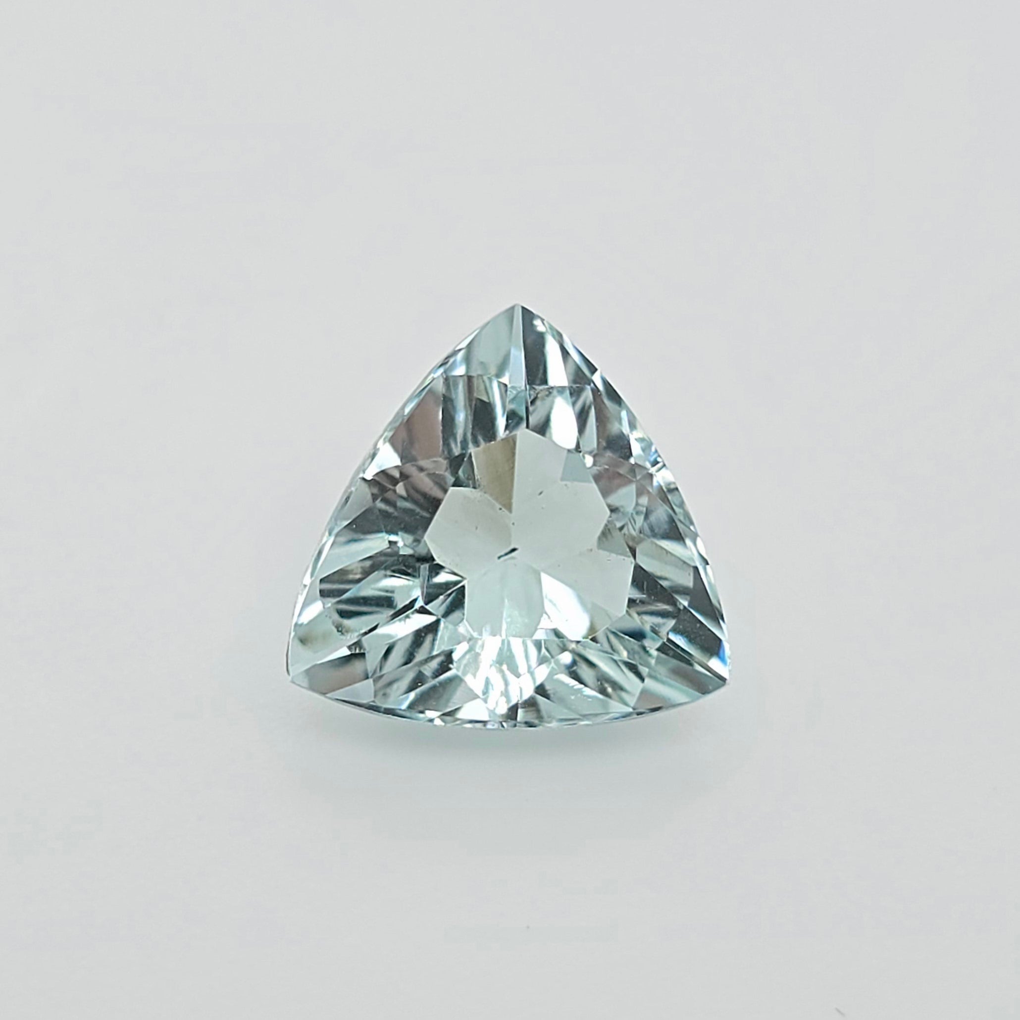 A single triangular faceted gemstone with a light blue-green hue, photographed on a clean light gray background.