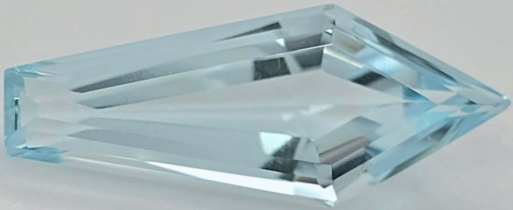 A faceted light blue gemstone with a pointed triangular end, shown on a neutral light gray background.
