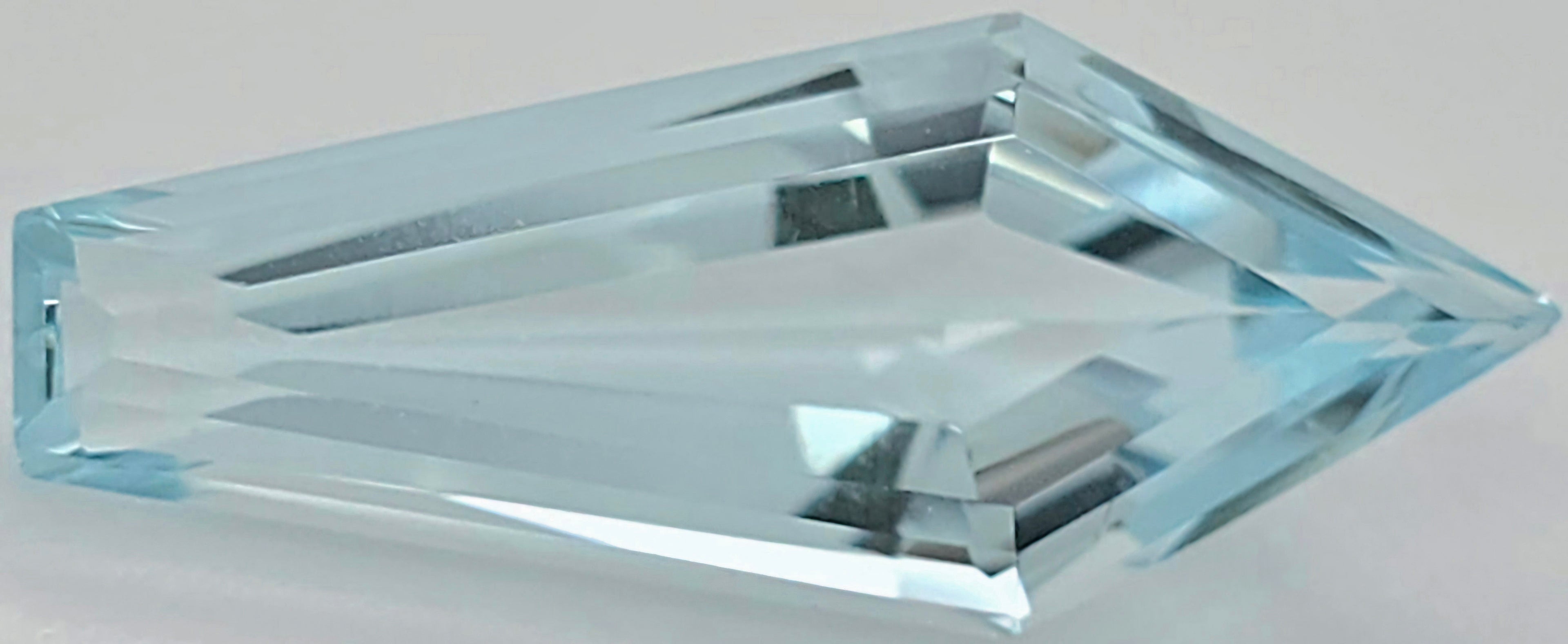 A faceted light blue gemstone with a pointed triangular end, shown on a neutral light gray background.