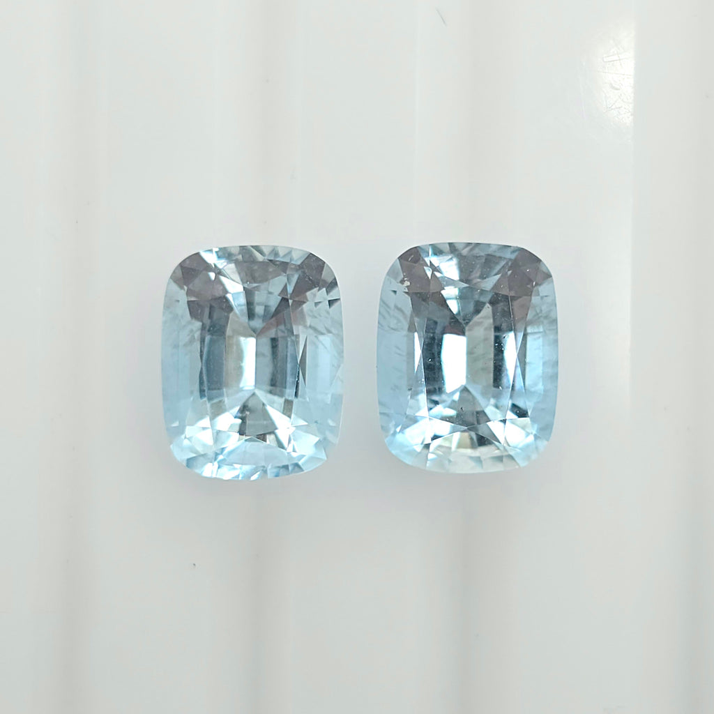 Two cushion-cut light blue gemstones displayed side by side on a clean white background.
