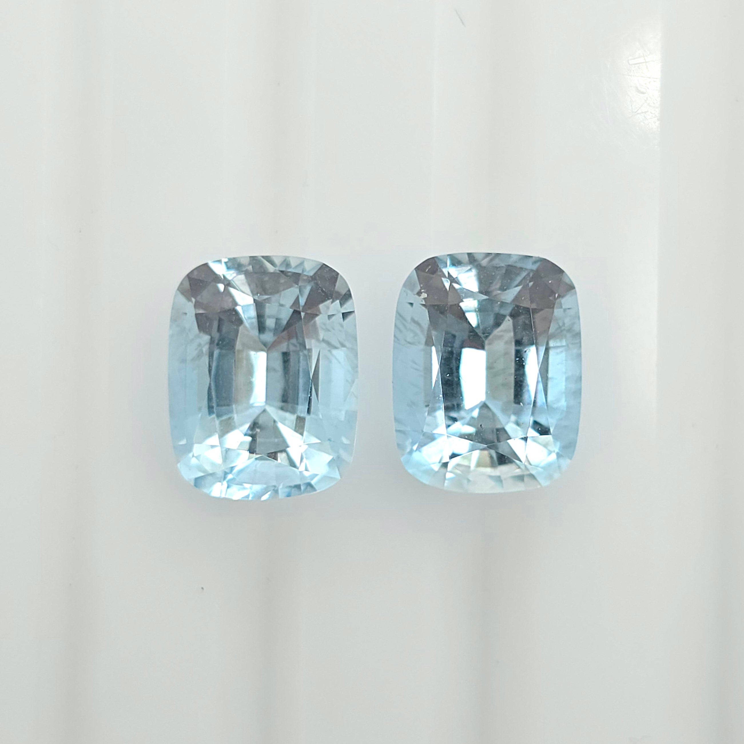 Two cushion-cut light blue gemstones displayed side by side on a clean white background.