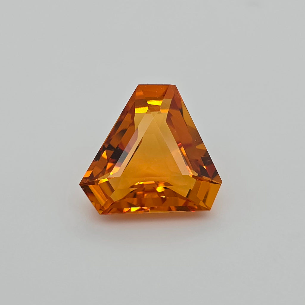 A faceted triangular orange gemstone, centered on a neutral light gray background.
