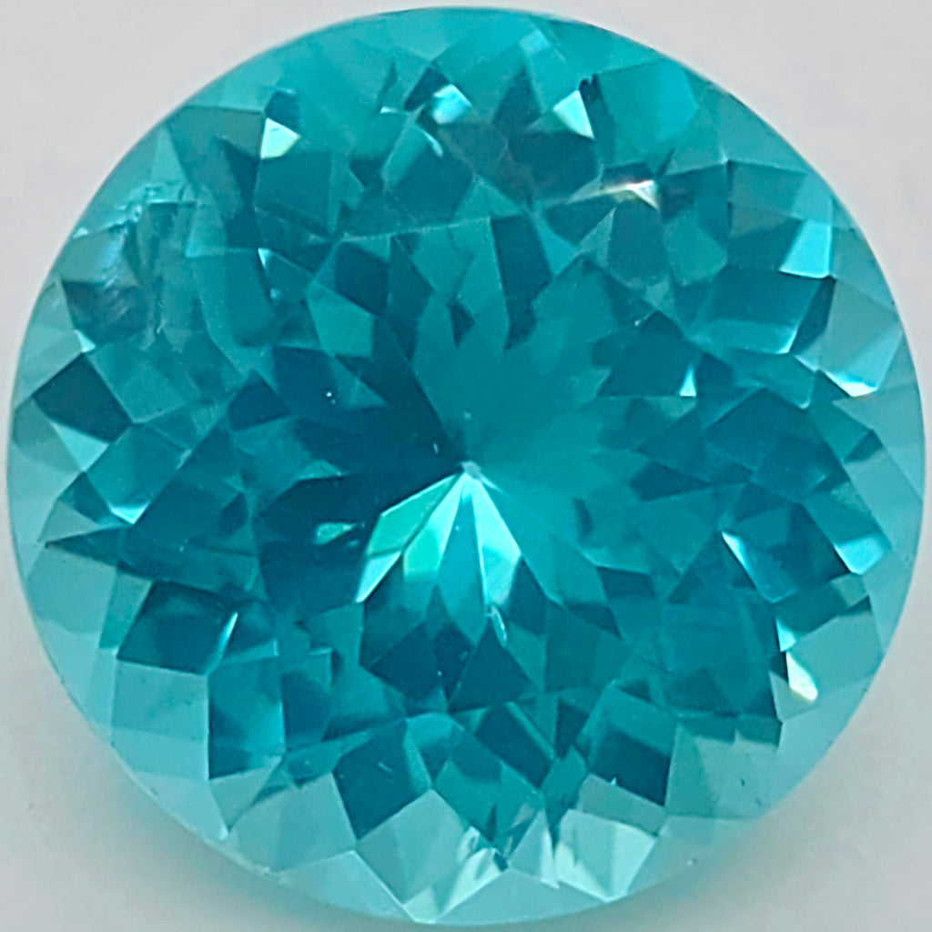 A round brilliant-cut turquoise gemstone showing vibrant blue-green facets against a plain light background.