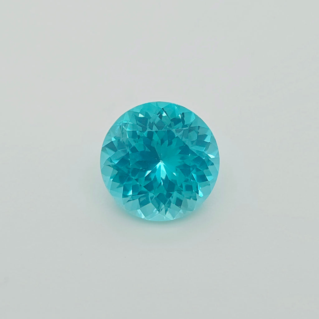 A round brilliant-cut greenish blue gemstone, centered on a plain light gray background.
