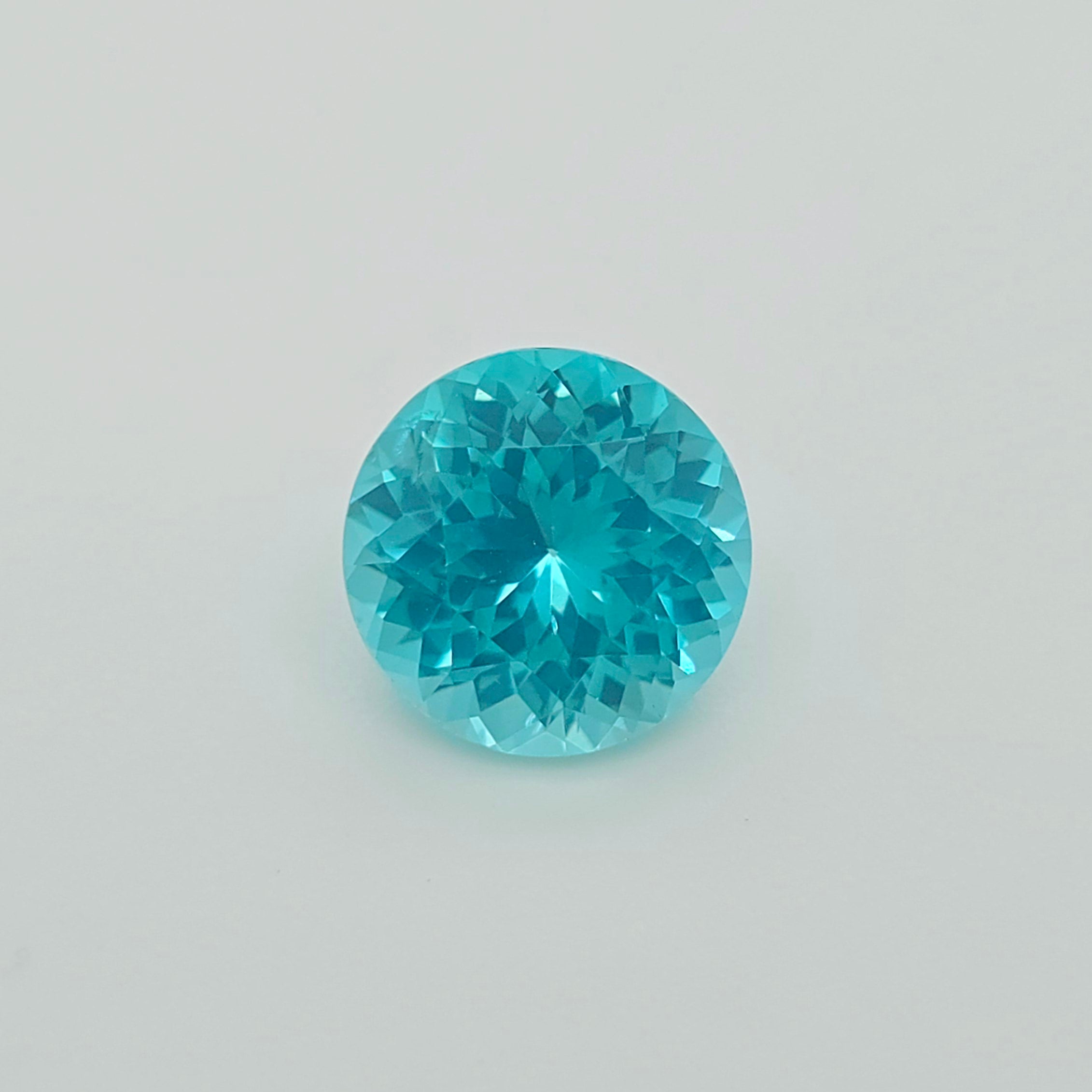 A round brilliant-cut greenish blue gemstone, centered on a plain light gray background.