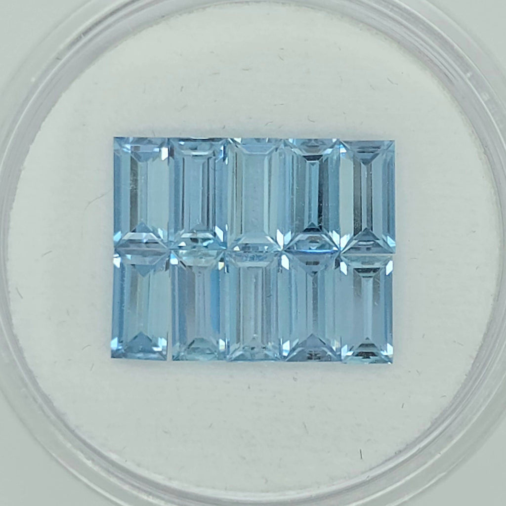 Ten rectangular baguette-cut light blue gemstone, displayed on a clean white surface inside a clear circular container.