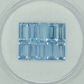 Ten rectangular baguette-cut light blue gemstone, displayed on a clean white surface inside a clear circular container.