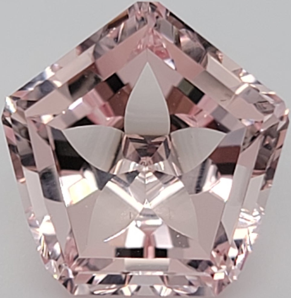 Close up of a pink pentagonal gemstone with flower pattern on a white background