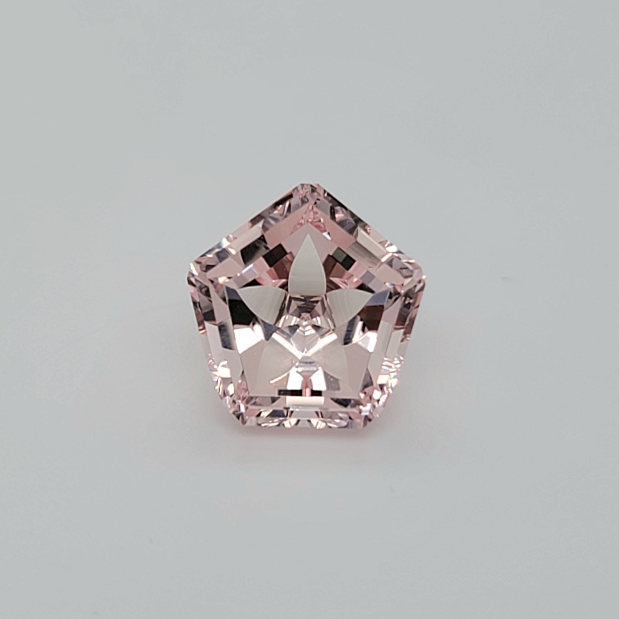 Pentagonal faceted gemstone with flower pattern on a lain white background