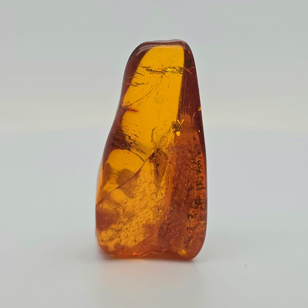 A polished amber stone with natural inclusions, standing upright on a light gray background.