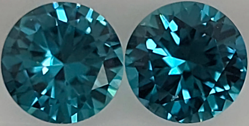 Two round brilliant-cut blue gemstones shown side by side against a plain light gray background.