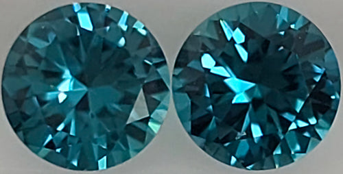 Two round brilliant-cut blue gemstones shown side by side against a plain light gray background.