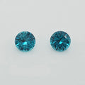 Two round-cut greenish blue gemstones on a plain light gray background.