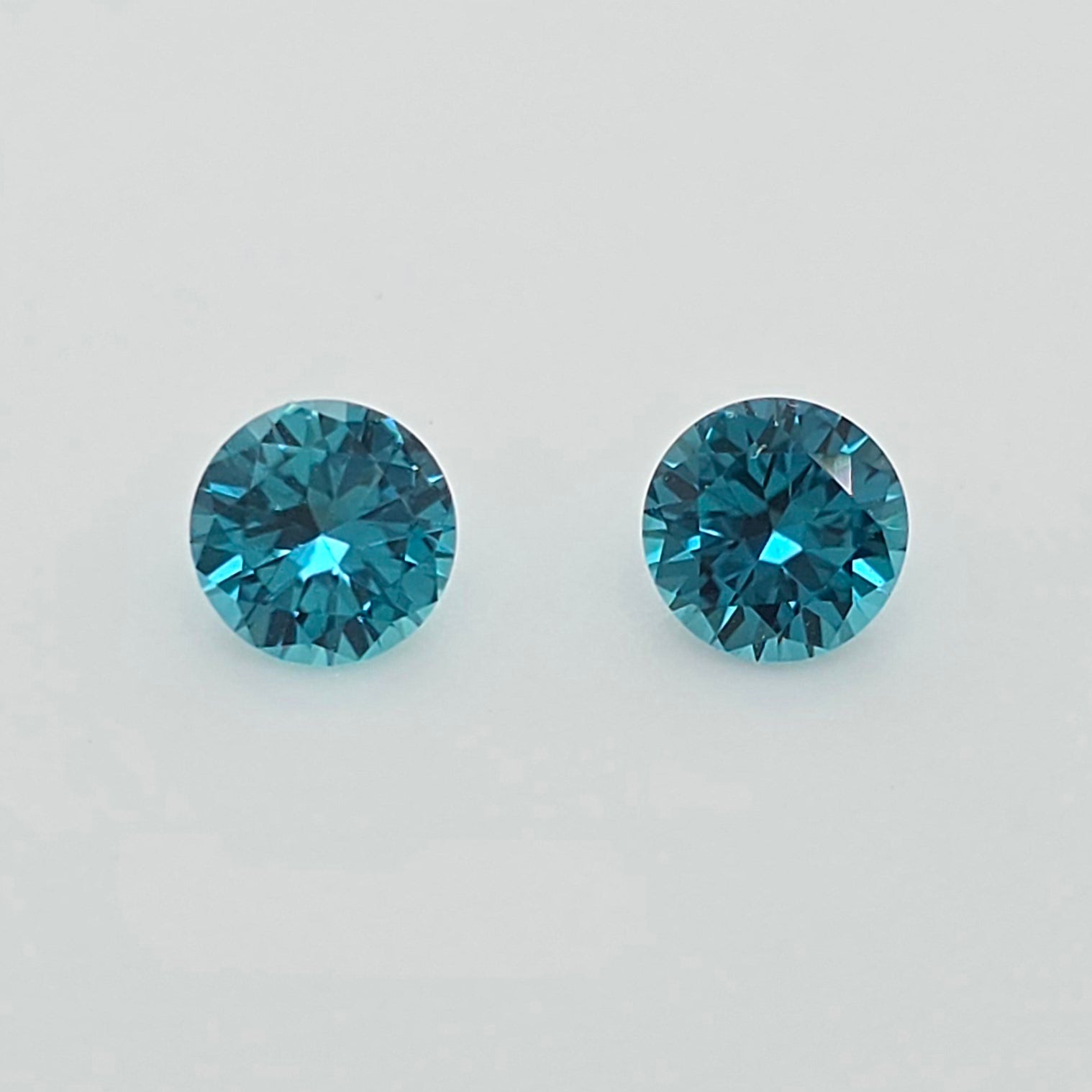 Two round-cut greenish blue gemstones on a plain light gray background.