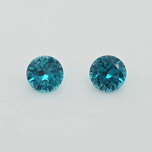 Two round-cut greenish blue gemstones on a plain light gray background.