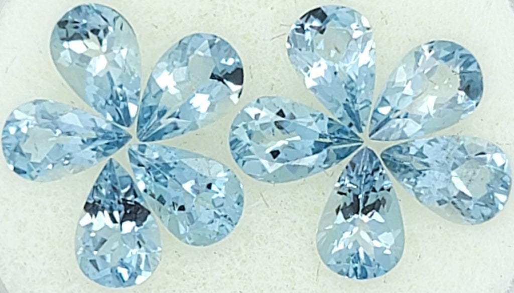 Close up image of ten pear shape light blue faceted stones arranged as two 5-petaled flowers on a plain white background