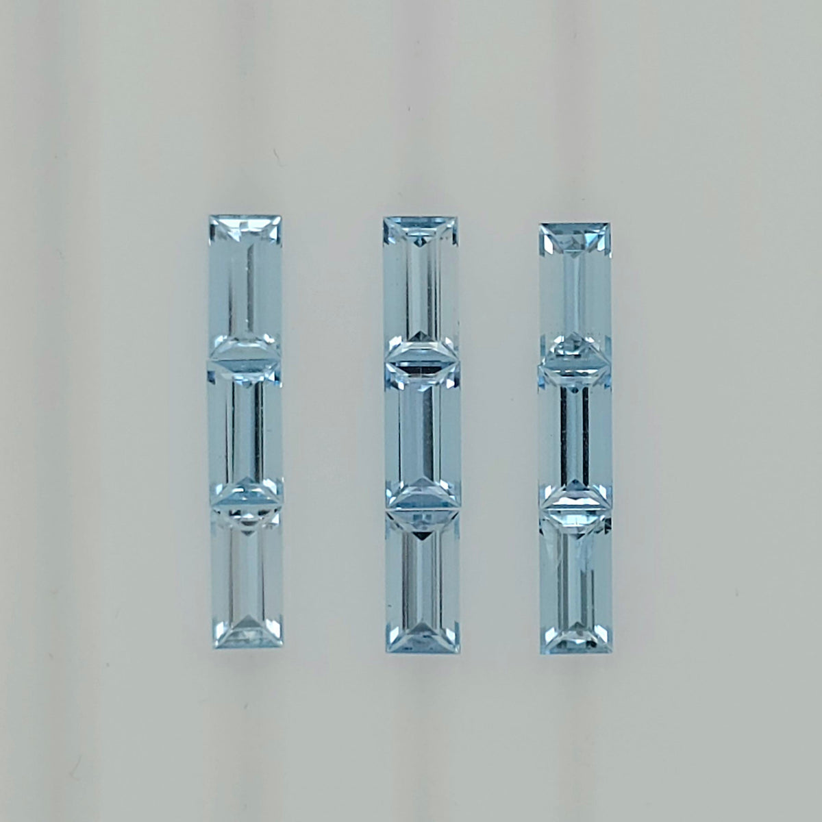 Image of nine rectangular light blue faceted stones arranged into three columns on a plain white background
