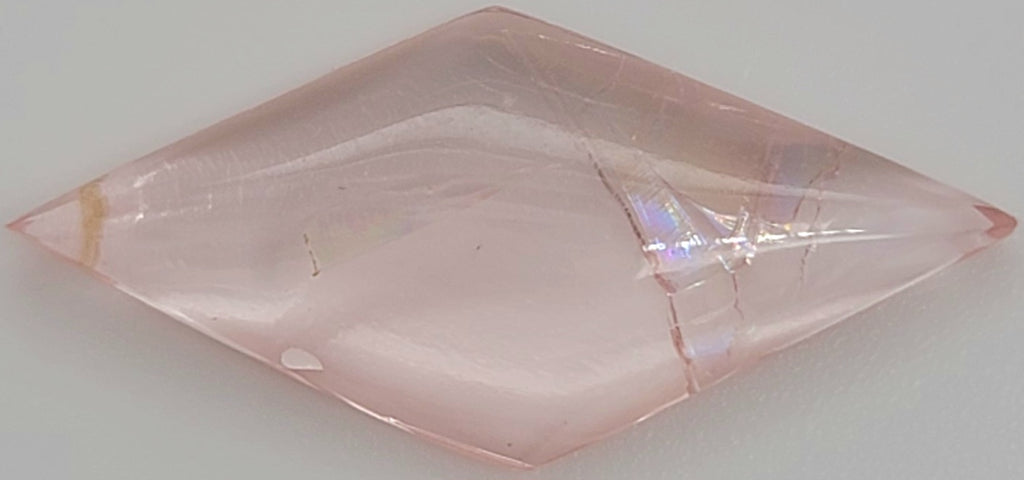 Close up of a diamond shaped pink cabochon gemstone with natural inclusions on a white background