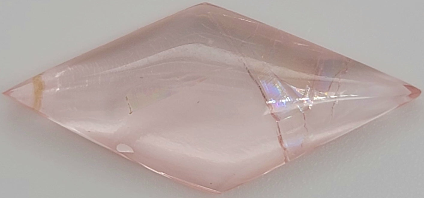 Close up of a diamond shaped pink cabochon gemstone with natural inclusions on a white background
