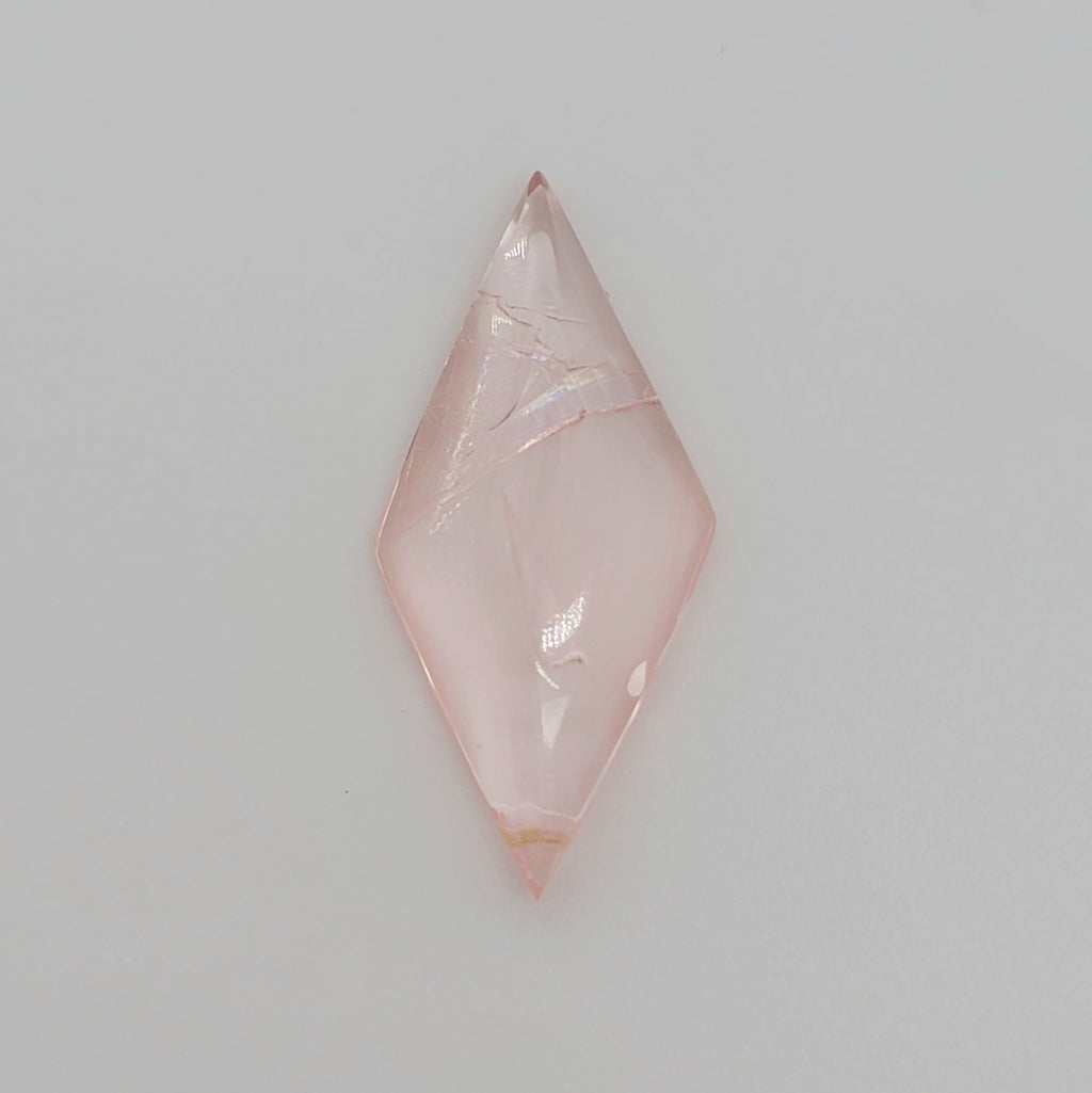 A diamond shaped pink gemstone cabochon with natural inclusions, displayed on a clean, light gray background.