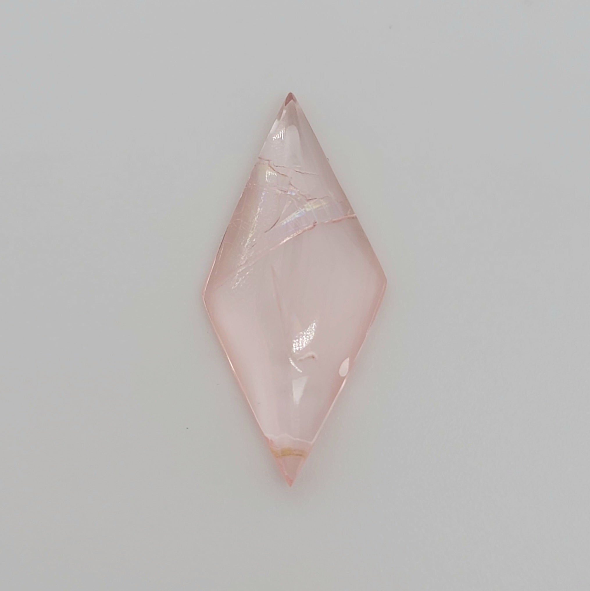 A diamond shaped pink gemstone cabochon with natural inclusions, displayed on a clean, light gray background.