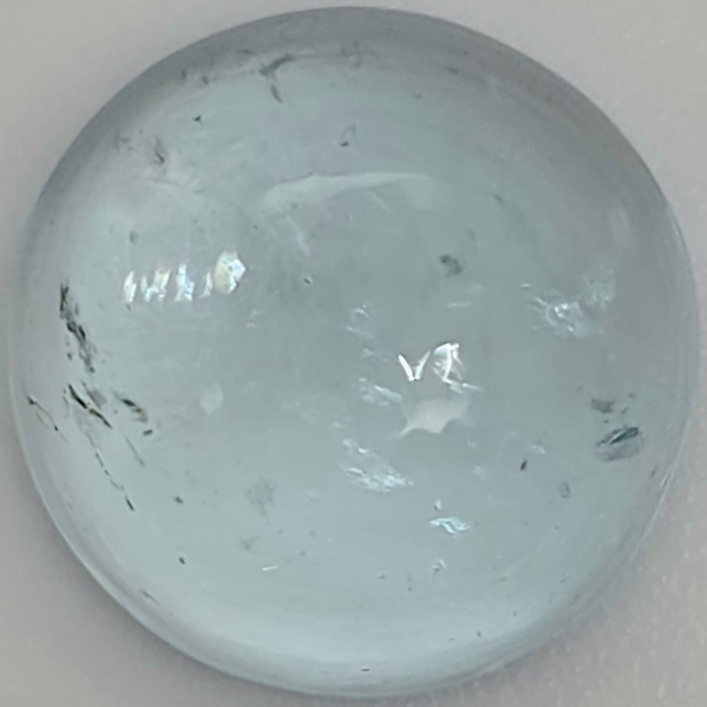 Close up of a light blue round domed gemstone with natural inclusions against a light background