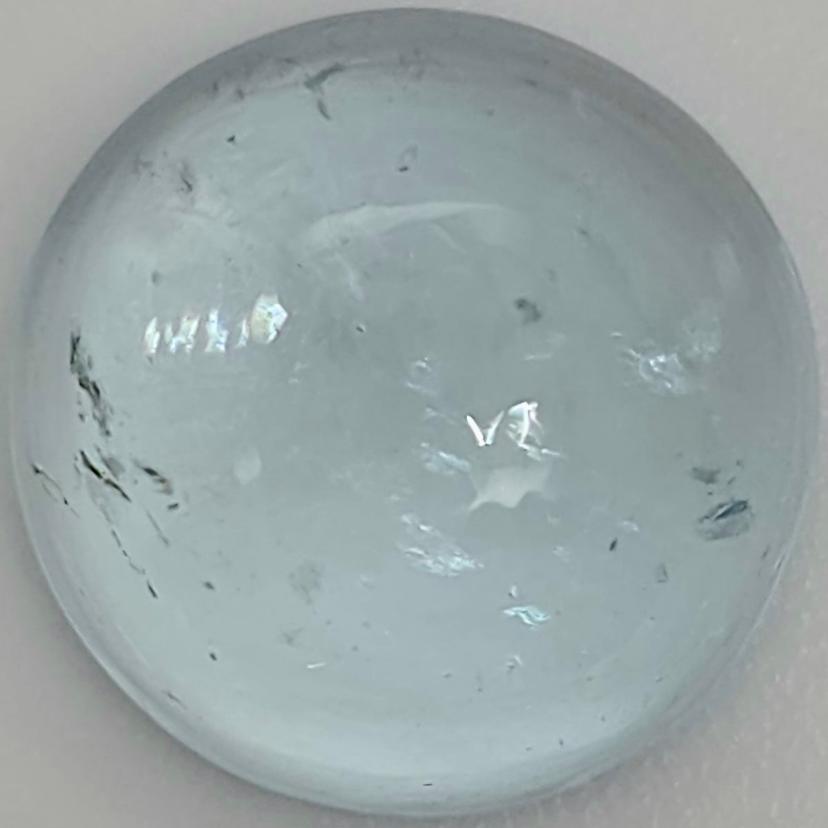 Close up of a light blue round domed gemstone with natural inclusions against a light background