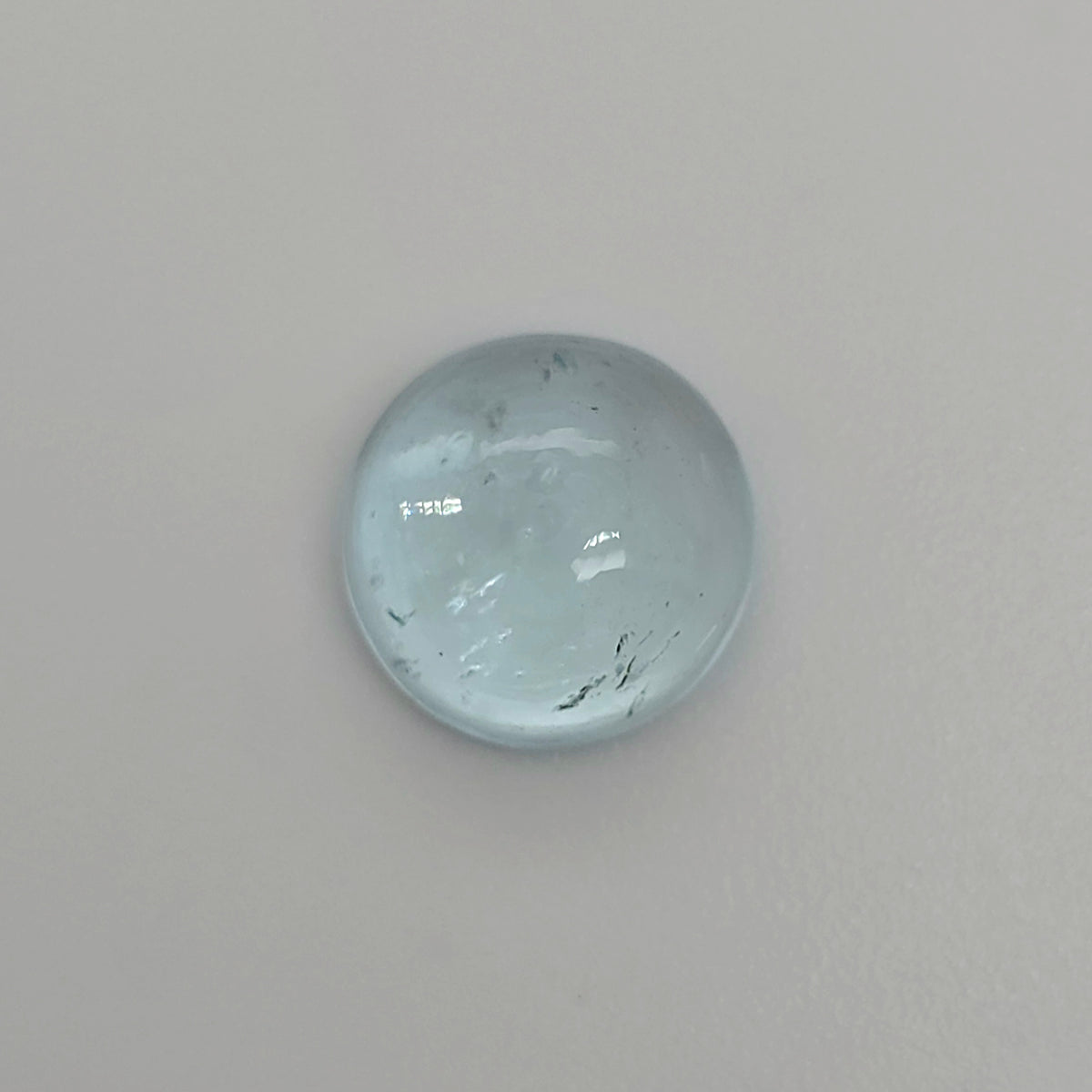 Round light blue domed gemstone against a light background