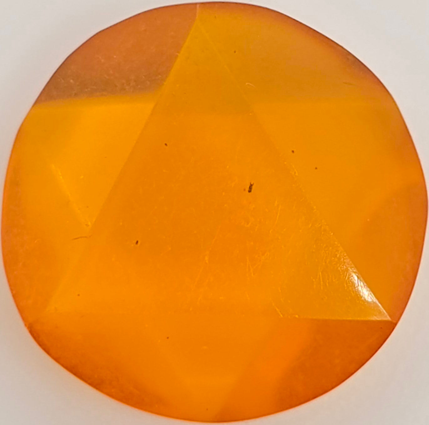 A faceted round orange gemstone on a plain white background.