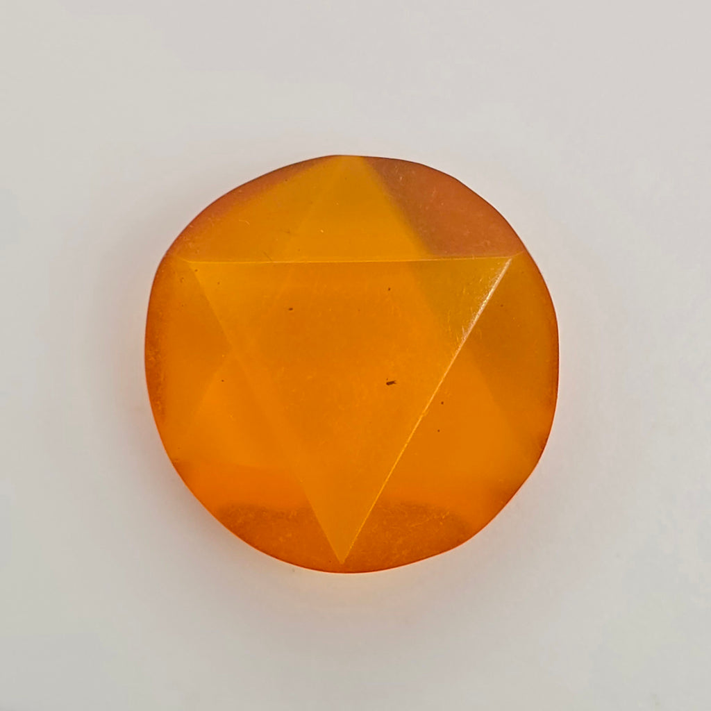 A single faceted orange gemstone with a circular shape and triangular cut facets, photographed on a plain light background.