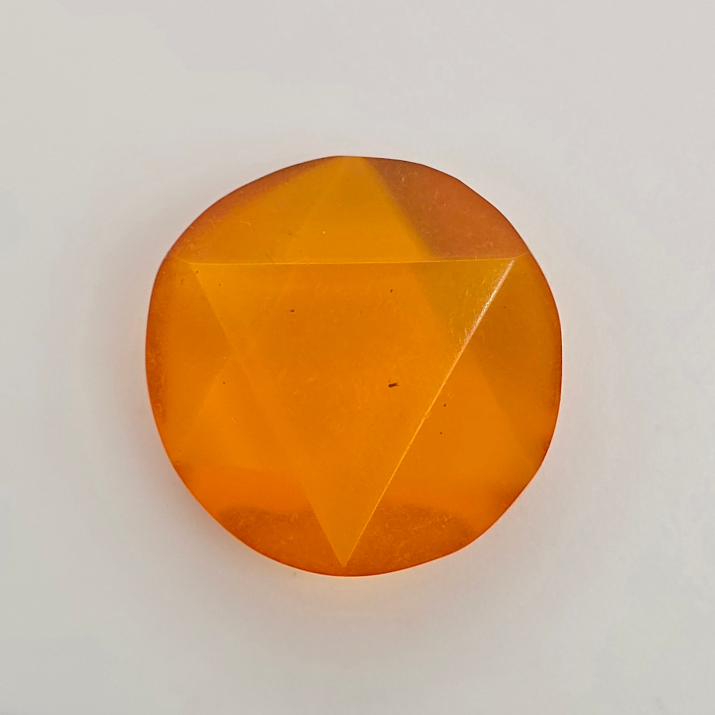 A single faceted orange gemstone with a circular shape and triangular cut facets, photographed on a plain light background.